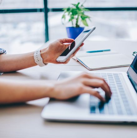 ISO management systems. Someone holding a phone and typing on a laptop working on their environmental systems.